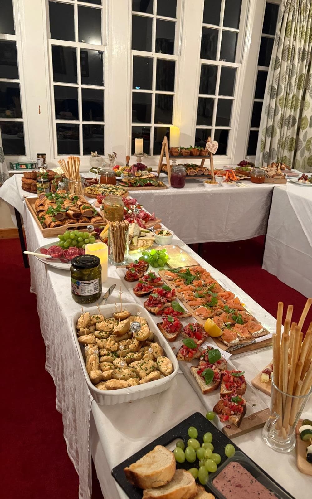 A buffet laid out by tall windows, with bruschetta, smoked salmon on toast and breadsticks in the foreground