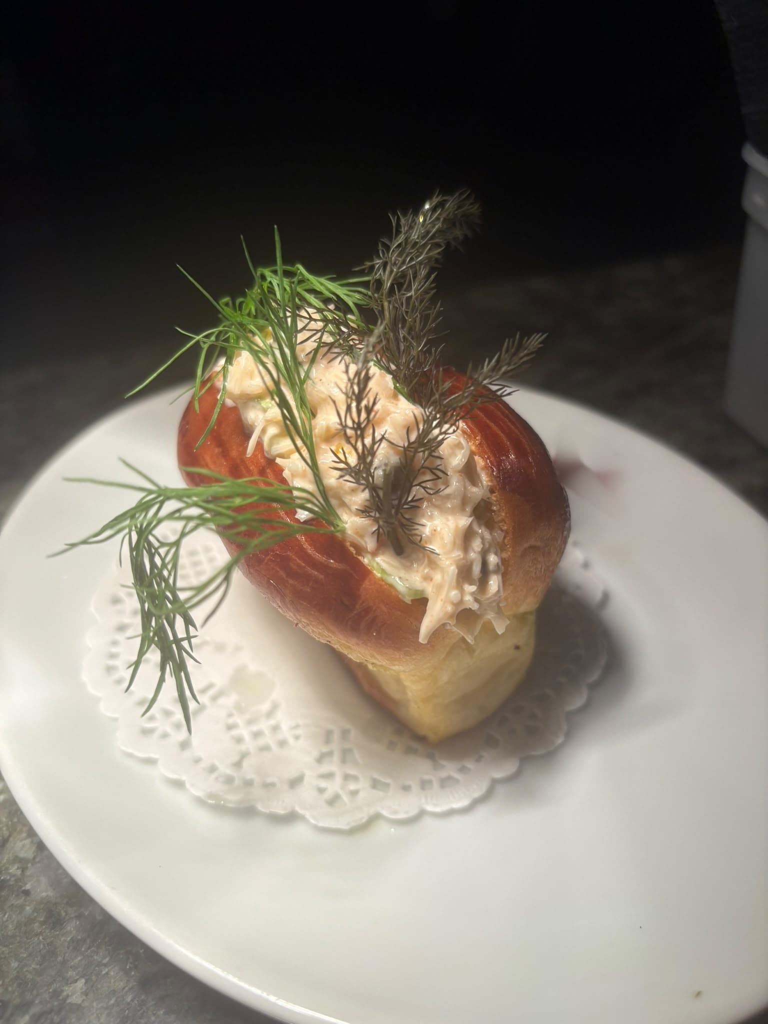 A glazed brioche roll filled with crab and topped with fresh herbs