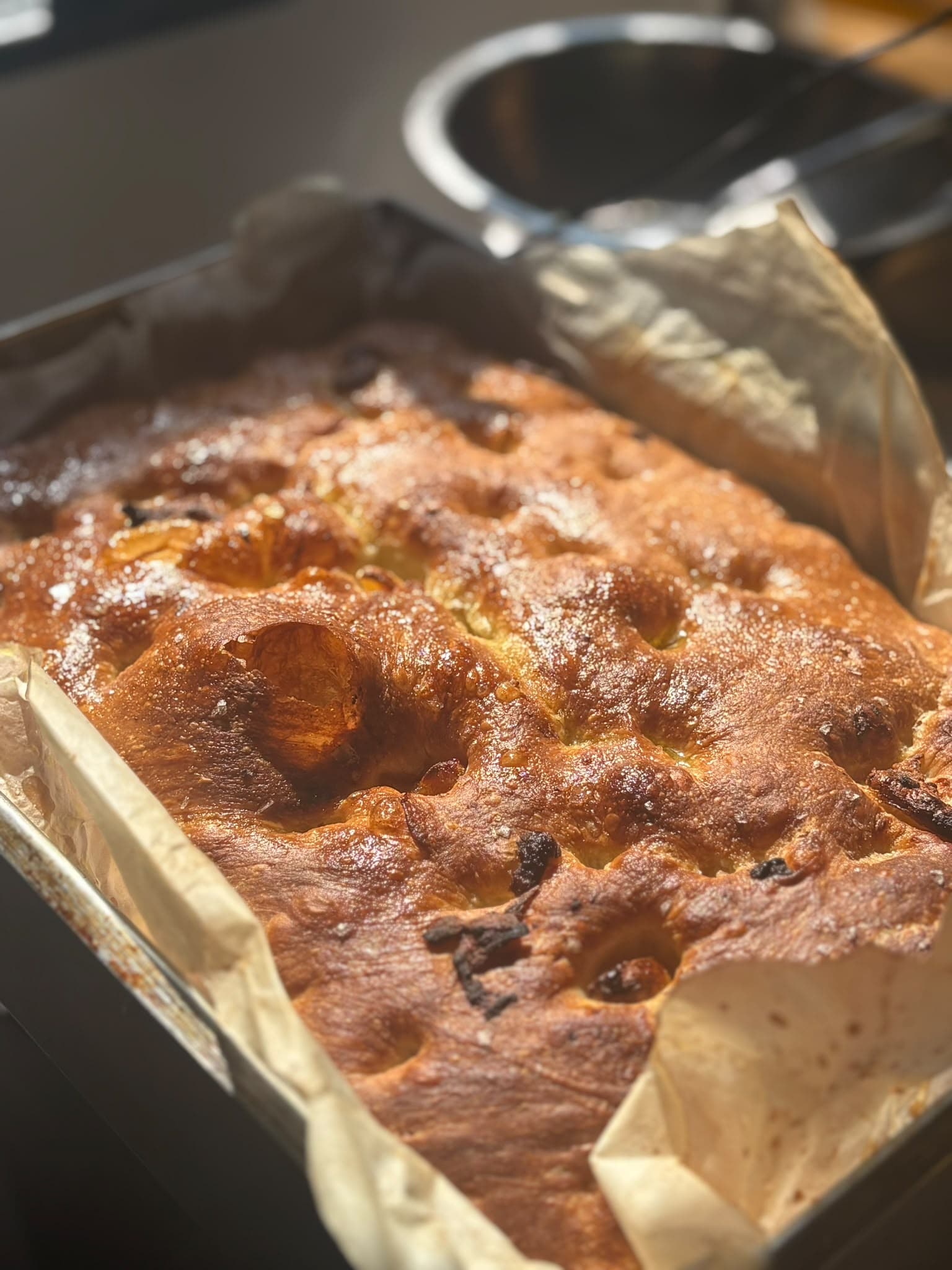 Golden focaccia fresh from the oven in a paper-lined tin