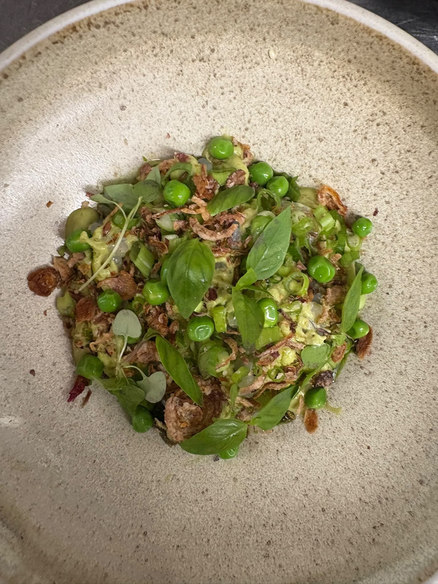 Fresh peas, basil leaves and crispy onions in a speckled stoneware bowl